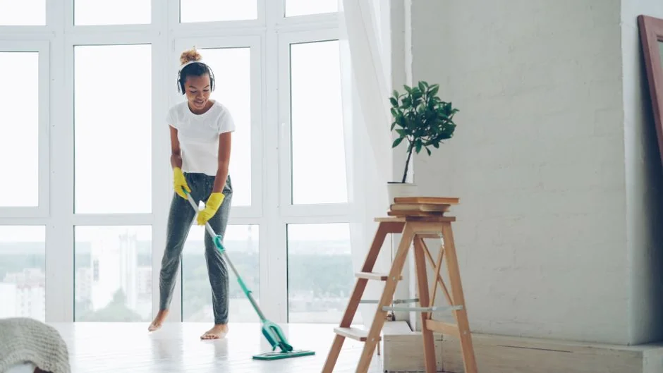 heros-img Two women in work clothes cleaning a modern living room using a vacuum and mop.